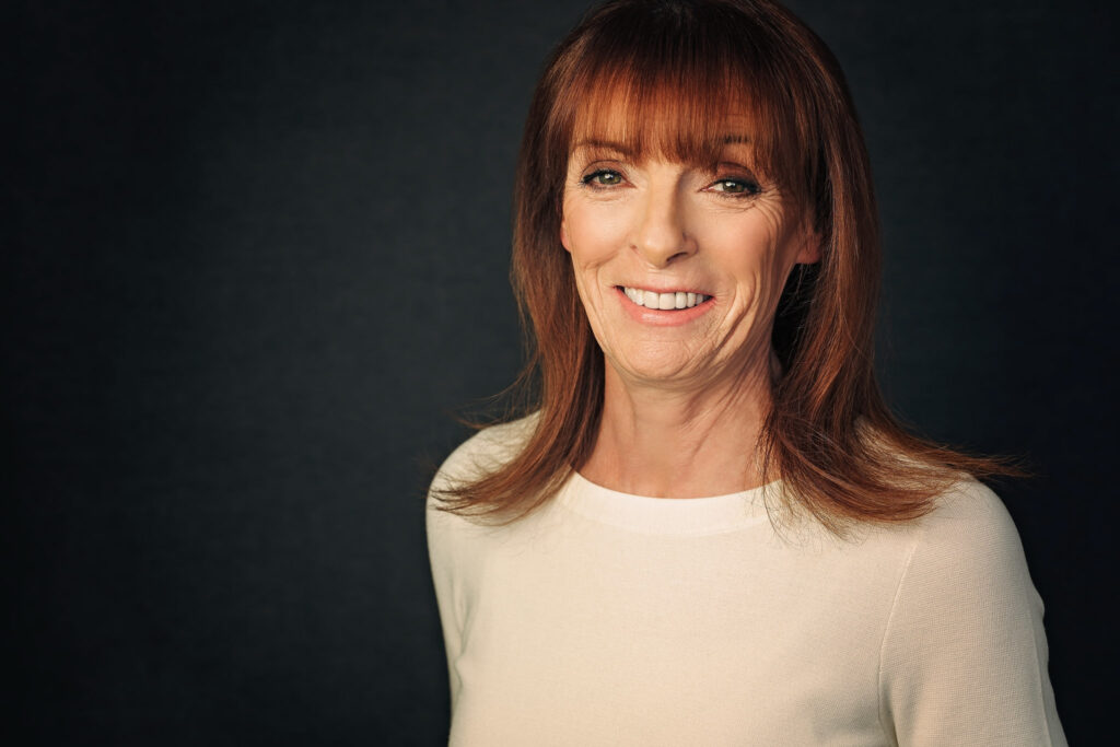 red headed female mature age headshot on grey paper wearing a cream sweater in studio